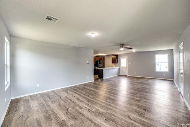 unfurnished living room with dark wood-type flooring, visible vents, ceiling fan, and baseboards