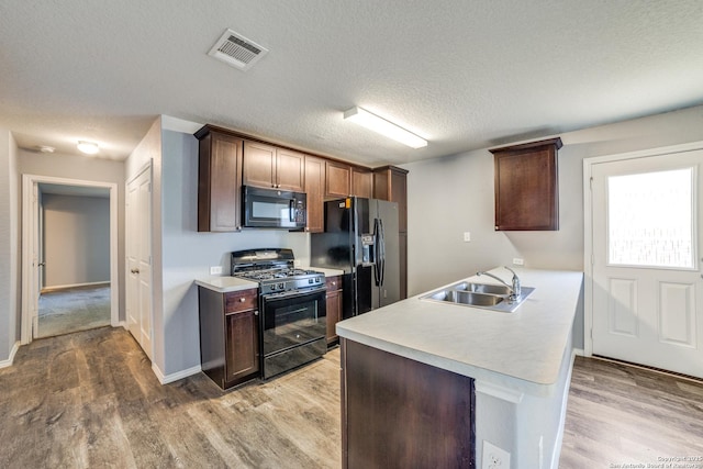 kitchen featuring visible vents, a sink, light countertops, black appliances, and light wood-style flooring