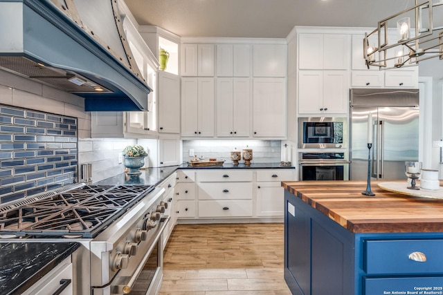 kitchen with butcher block countertops, under cabinet range hood, built in appliances, and white cabinetry