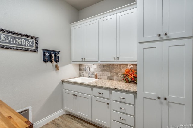 kitchen featuring baseboards, a sink, light wood-type flooring, white cabinetry, and backsplash