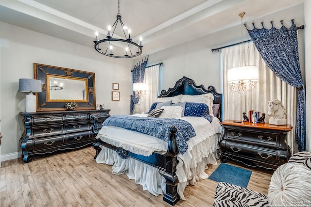 bedroom featuring an inviting chandelier, a tray ceiling, ornamental molding, wood finished floors, and baseboards