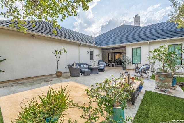 rear view of house with stucco siding, a chimney, an outdoor living space, a patio area, and a tile roof