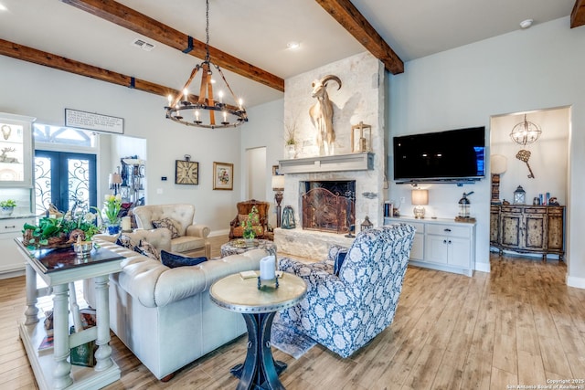 living room with visible vents, light wood-type flooring, an inviting chandelier, and beam ceiling