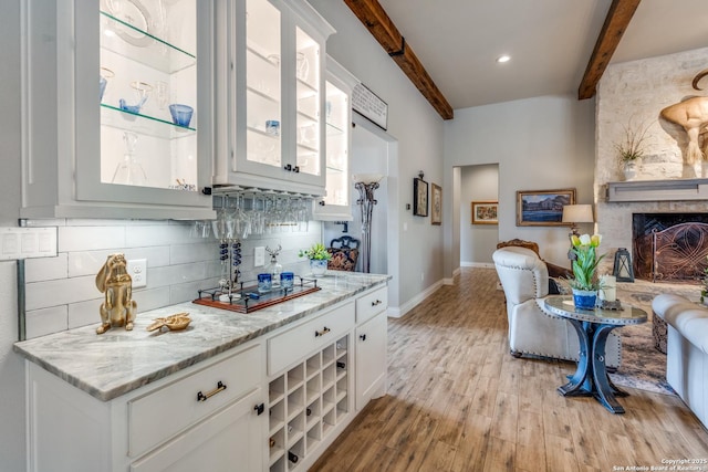 kitchen featuring light wood-style floors, beamed ceiling, glass insert cabinets, decorative backsplash, and baseboards
