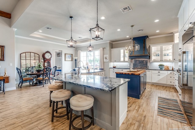 kitchen with butcher block countertops, premium range hood, a large island with sink, and visible vents