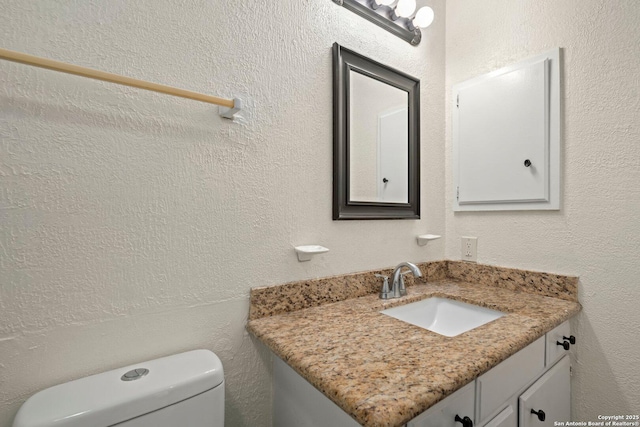 half bath featuring a textured wall, vanity, and toilet