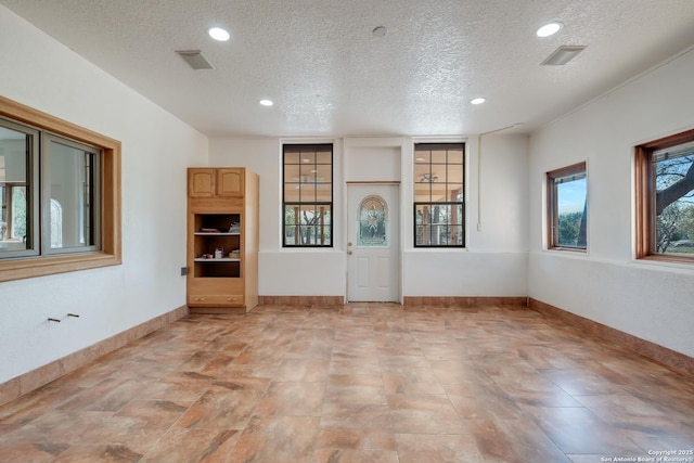 unfurnished living room with a textured ceiling, baseboards, and recessed lighting