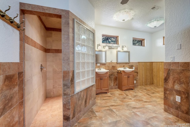 full bath featuring a textured ceiling, a walk in shower, wainscoting, tile walls, and a sink