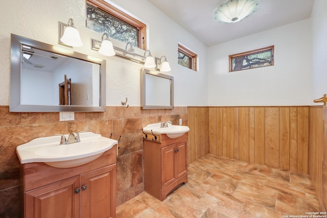 full bath featuring a sink, a wainscoted wall, and two vanities