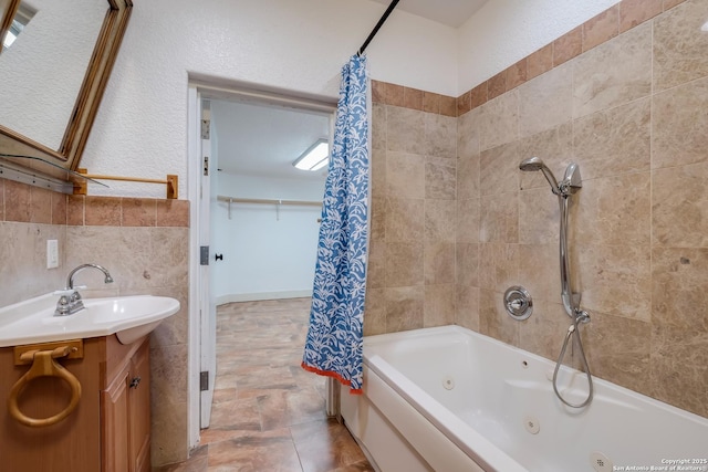 bathroom with a combined bath / shower with jetted tub, vanity, and tile walls