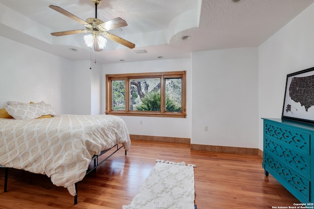 bedroom featuring a raised ceiling, a textured ceiling, wood finished floors, and baseboards