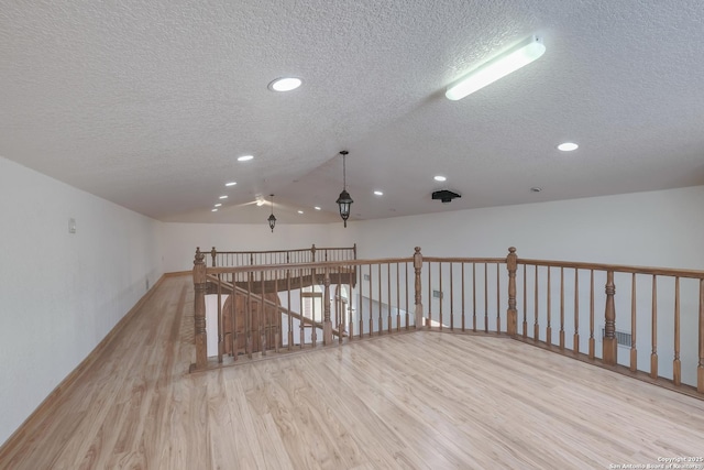 empty room with a textured ceiling, recessed lighting, wood finished floors, lofted ceiling, and baseboards