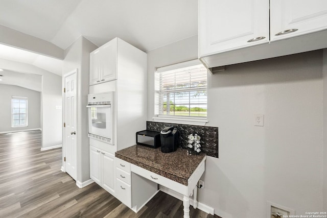kitchen with white oven, white cabinets, dark wood-style flooring, lofted ceiling, and baseboards