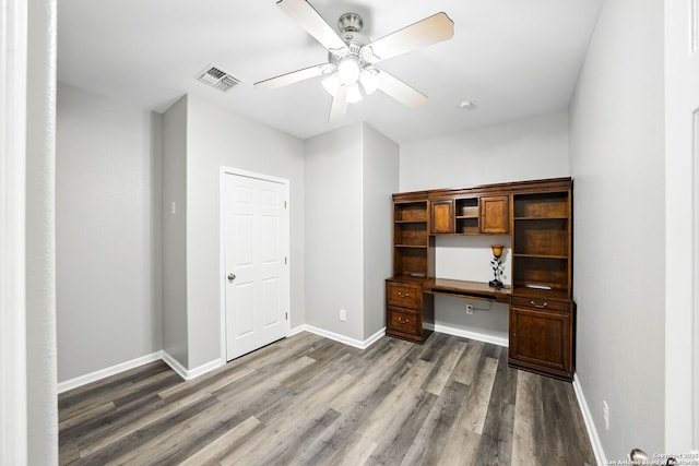 unfurnished office with baseboards, built in study area, a ceiling fan, dark wood-type flooring, and visible vents