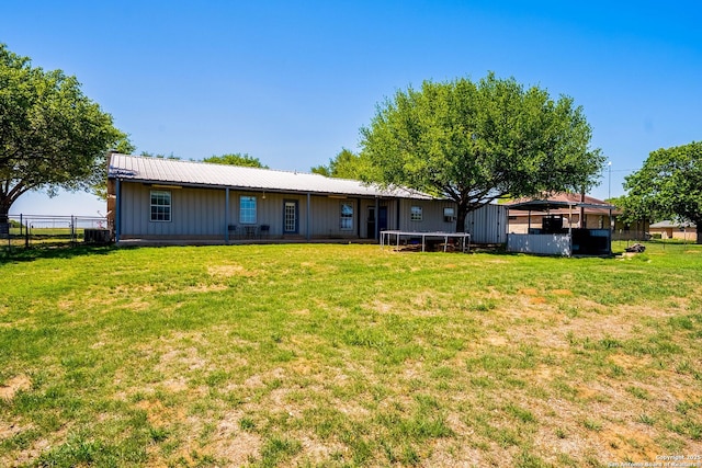 rear view of house featuring a trampoline, board and batten siding, a yard, metal roof, and fence