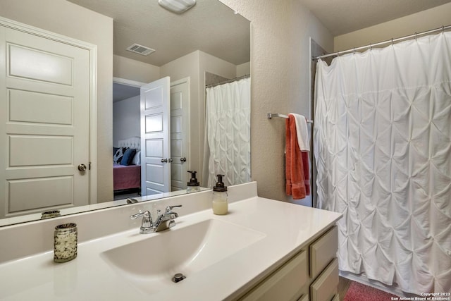 full bathroom with vanity, a textured wall, ensuite bath, a textured ceiling, and visible vents
