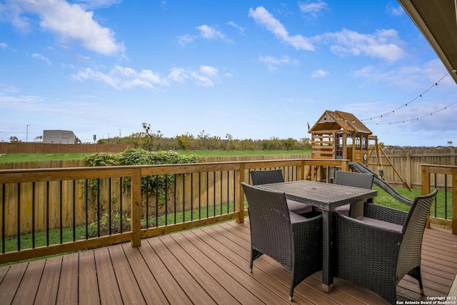deck with outdoor dining space, fence, and a playground