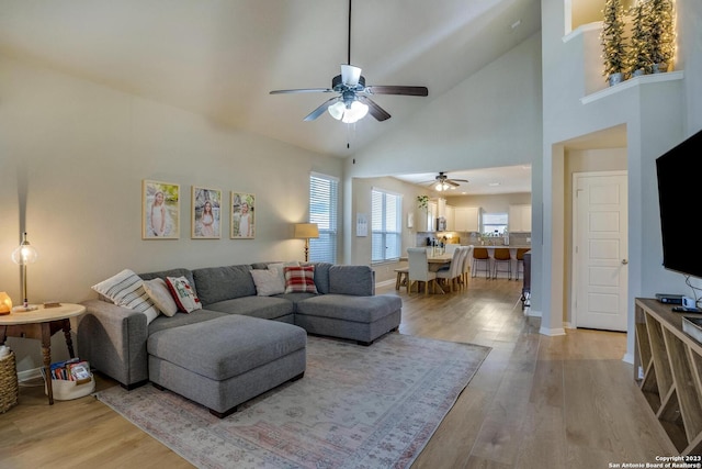 living room with high vaulted ceiling, light wood-style floors, baseboards, and ceiling fan
