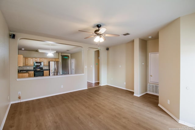 unfurnished living room featuring arched walkways, light wood finished floors, a sink, and a ceiling fan