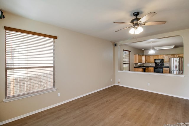 unfurnished living room with a sink, baseboards, a ceiling fan, and wood finished floors