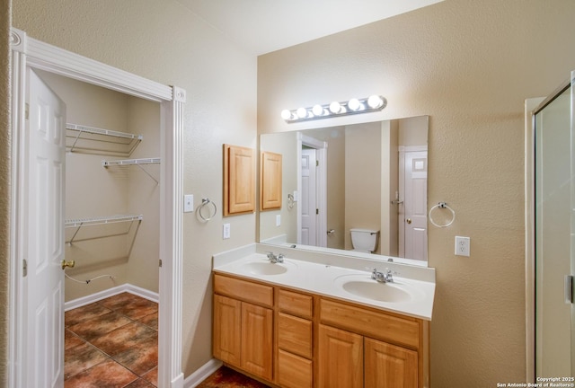 bathroom with a walk in closet, double vanity, a sink, and toilet
