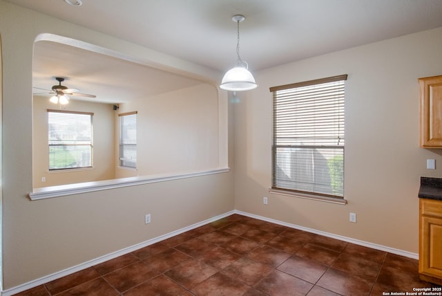 unfurnished dining area with dark tile patterned floors, baseboards, and a ceiling fan