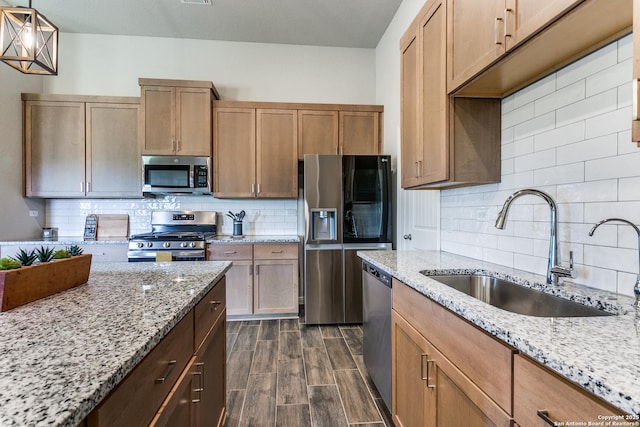 kitchen with light stone countertops, wood finish floors, appliances with stainless steel finishes, a sink, and decorative backsplash