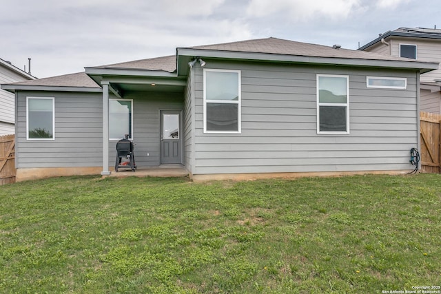 back of property featuring a shingled roof, fence, and a lawn