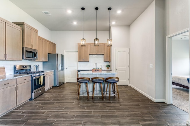 kitchen featuring a kitchen breakfast bar, wood finish floors, a kitchen island, stainless steel appliances, and pendant lighting