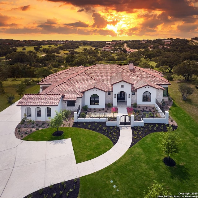 mediterranean / spanish house featuring stucco siding, a chimney, a fenced front yard, a front yard, and a tiled roof