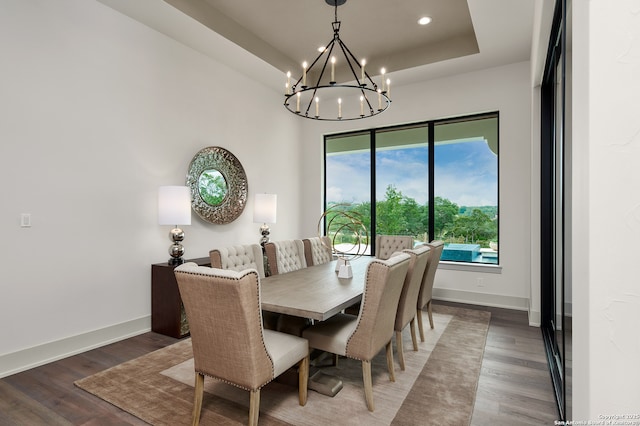 dining space with a raised ceiling, wood finished floors, an inviting chandelier, and baseboards