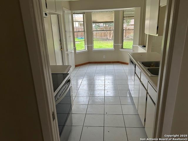 7834 Sun Frst, San Antonio, TX 78239 - kitchen featuring light tile patterned floors, electric range, white cabinets, a sink, and baseboards