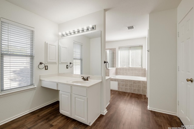 bathroom with wood finished floors, vanity, a garden tub, and visible vents