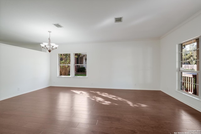 empty room featuring a healthy amount of sunlight, a notable chandelier, dark wood finished floors, and visible vents