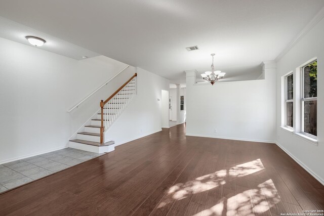 unfurnished living room featuring visible vents, a chandelier, wood finished floors, stairs, and baseboards