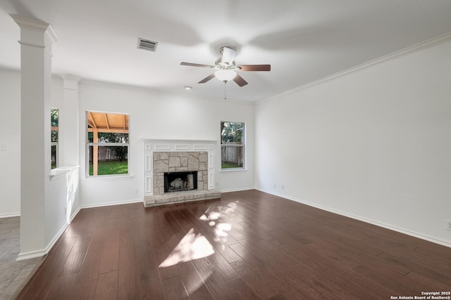 unfurnished living room featuring visible vents, ceiling fan, a stone fireplace, ornate columns, and dark wood-type flooring