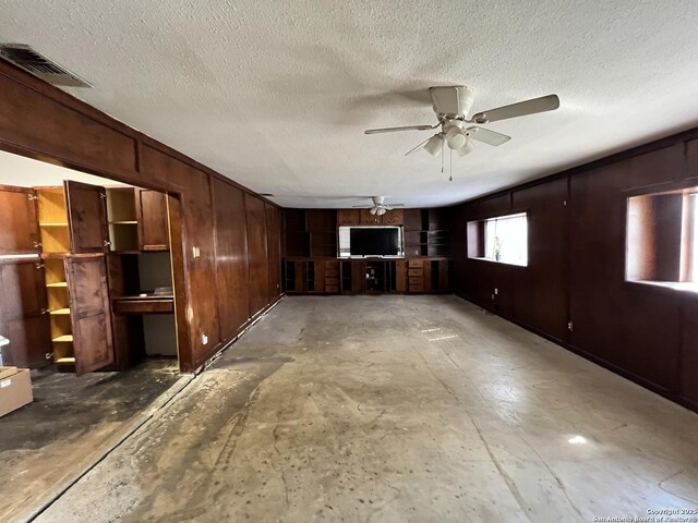 5874 Castle Hunt, San Antonio, TX 78218 - unfurnished living room with wooden walls, visible vents, a ceiling fan, and a textured ceiling