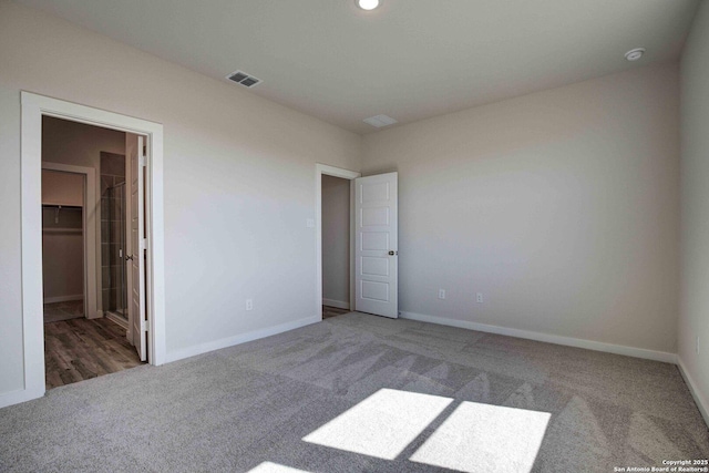 unfurnished bedroom with visible vents, baseboards, a walk in closet, and carpet