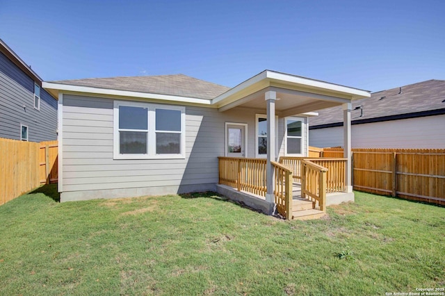 rear view of house with a fenced backyard, a lawn, and roof with shingles
