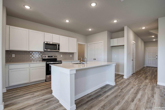 kitchen with white cabinetry, appliances with stainless steel finishes, light countertops, a sink, and light wood finished floors