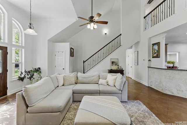 living room featuring baseboards, stairway, finished concrete flooring, a high ceiling, and ceiling fan