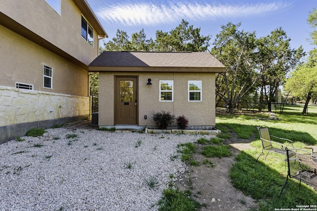doorway to property featuring a shingled roof, stucco siding, fence, and a lawn