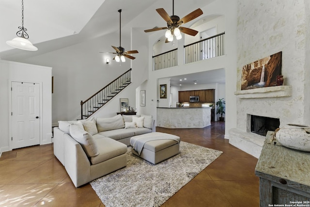 living area featuring a ceiling fan, stairs, dark tile patterned flooring, high vaulted ceiling, and a premium fireplace