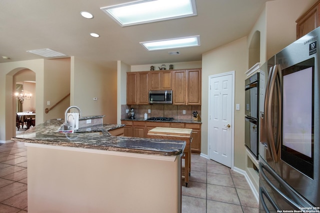 kitchen featuring light tile patterned floors, arched walkways, a large island, stainless steel appliances, and decorative backsplash