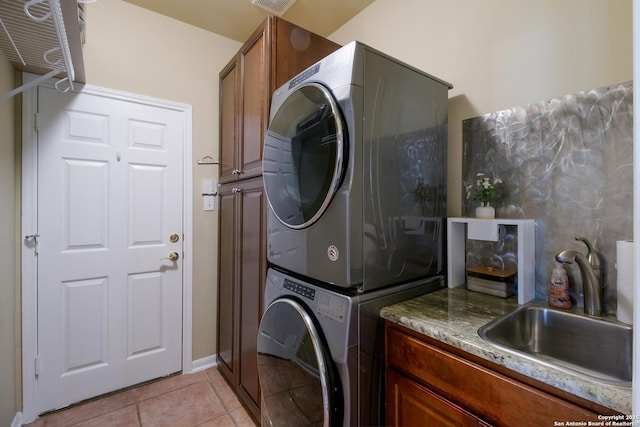 laundry room with stacked washer and dryer, light tile patterned floors, visible vents, cabinet space, and a sink
