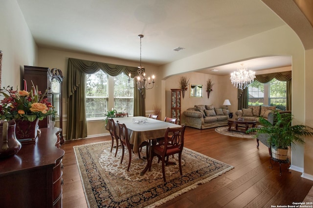 dining room featuring a chandelier, arched walkways, dark wood-style floors, and a healthy amount of sunlight