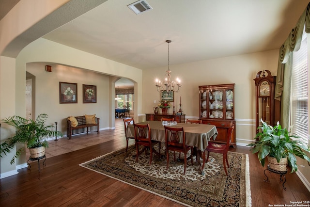 dining room with an inviting chandelier, arched walkways, visible vents, wood-type flooring, and baseboards