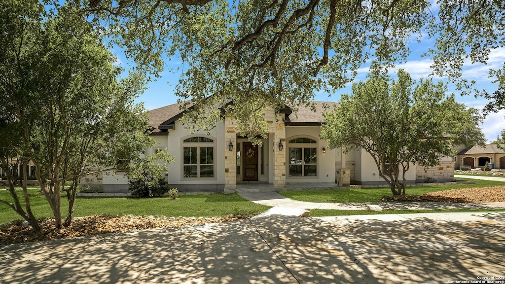 view of front of house featuring a front yard, roof with shingles, and stucco siding
