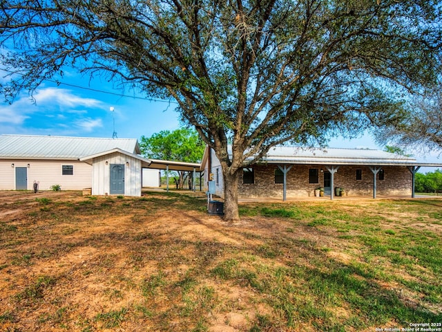 601 Wildflower Dr, Lytle, TX 78052 - rear view of property with a yard, stone siding, an attached carport, and an outbuilding