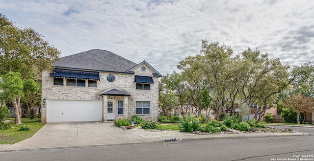 french provincial home with an attached garage, driveway, and brick siding